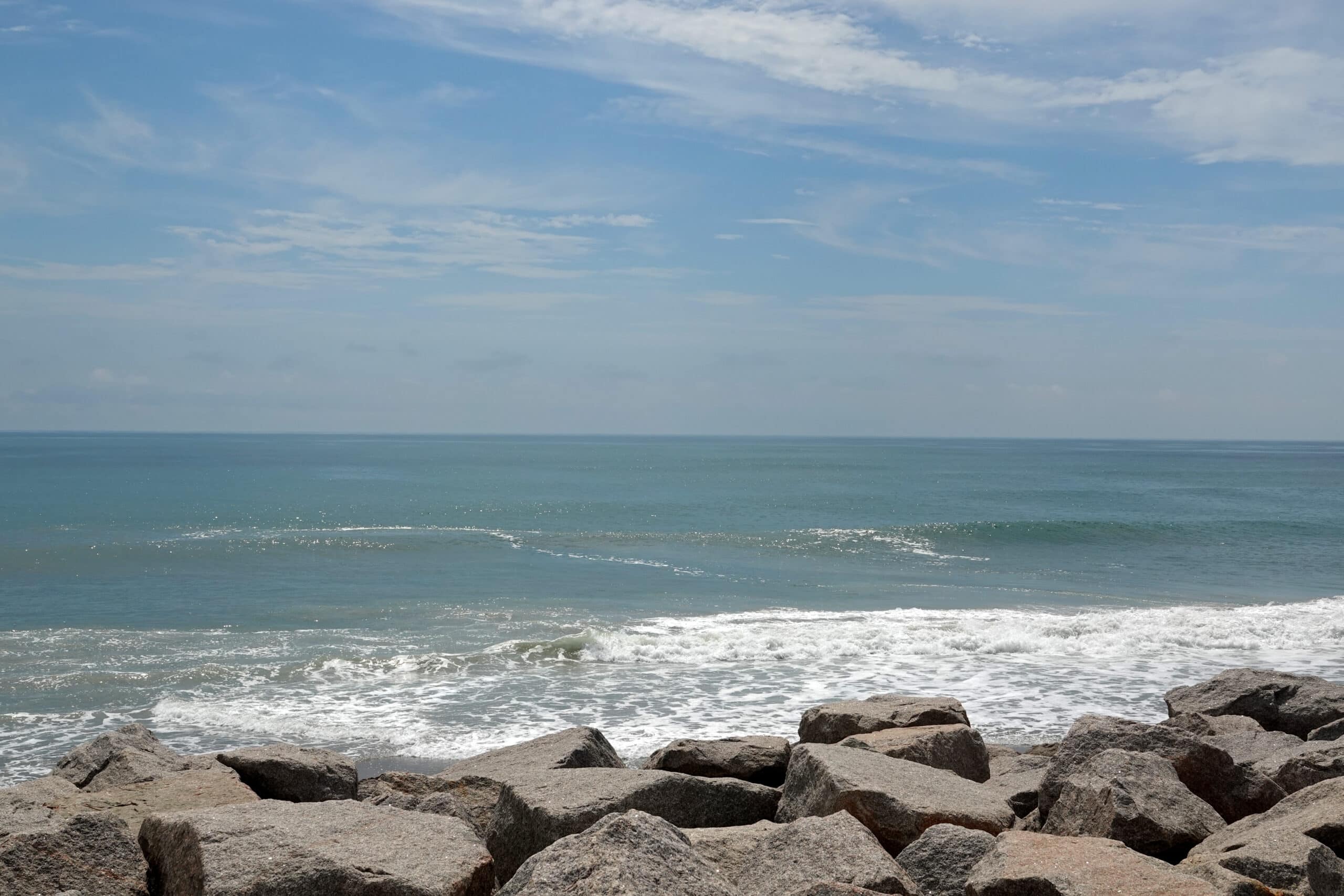 Rip current at Fort Fisher, North Carolina, visible as a flat gap in the breaking surf just past the rock revetment.