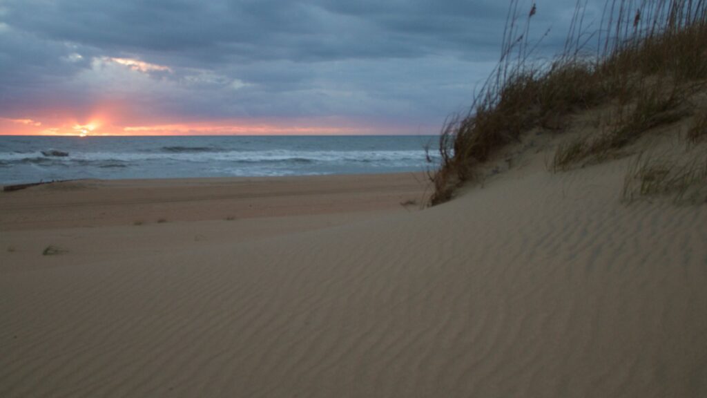 An autumn sunrise breaking over the ocean beyond a low sand dune at Cape Hatteras National Seashore.