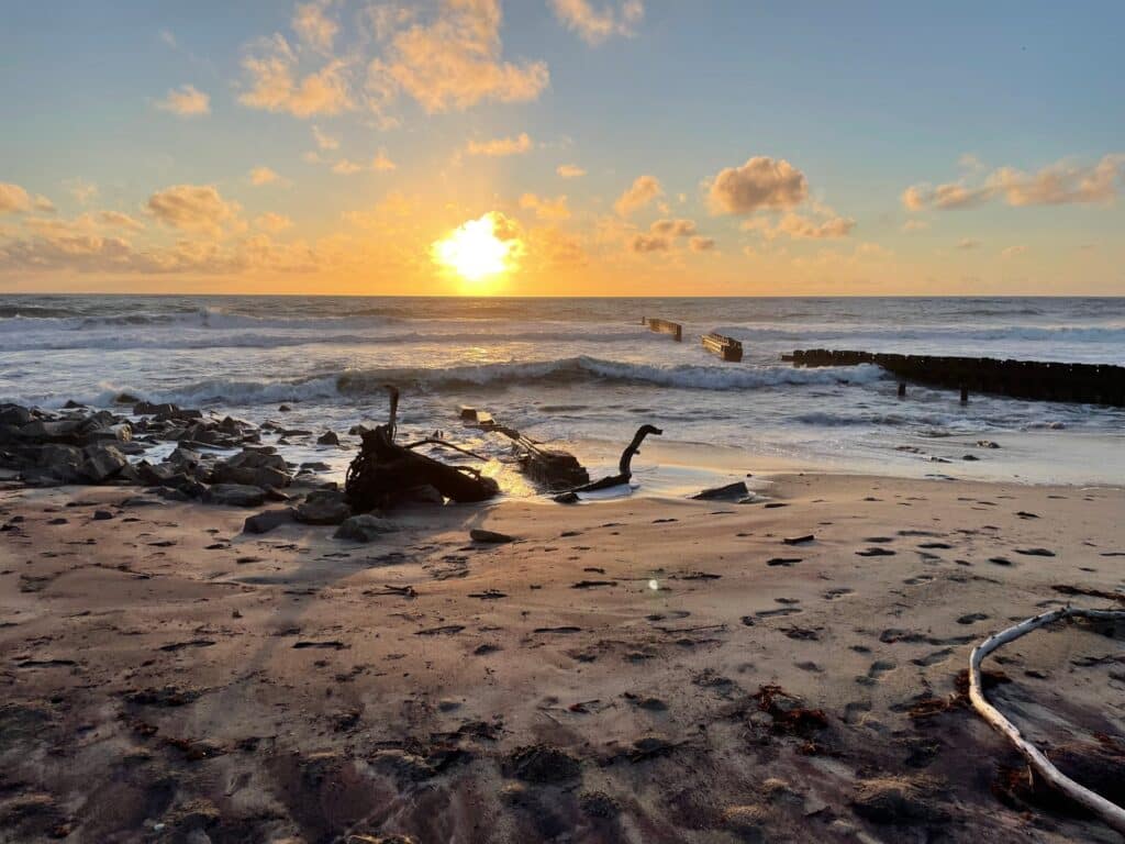 Sunrise over the ocean with driftwood and wet sand in the foreground at the Buxton beach access.