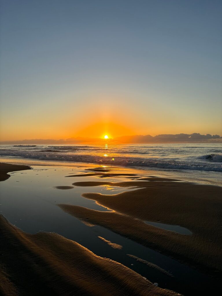 Sunrise reflected in a shallow tidal pool on a wide, flat beach at Ocracoke Island.