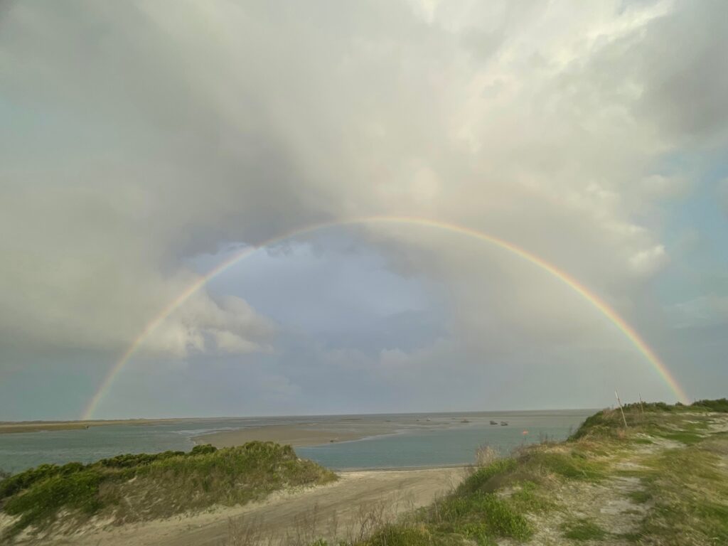 A broad rainbow arcing over the grass and shallow water of Pamlico Sound.