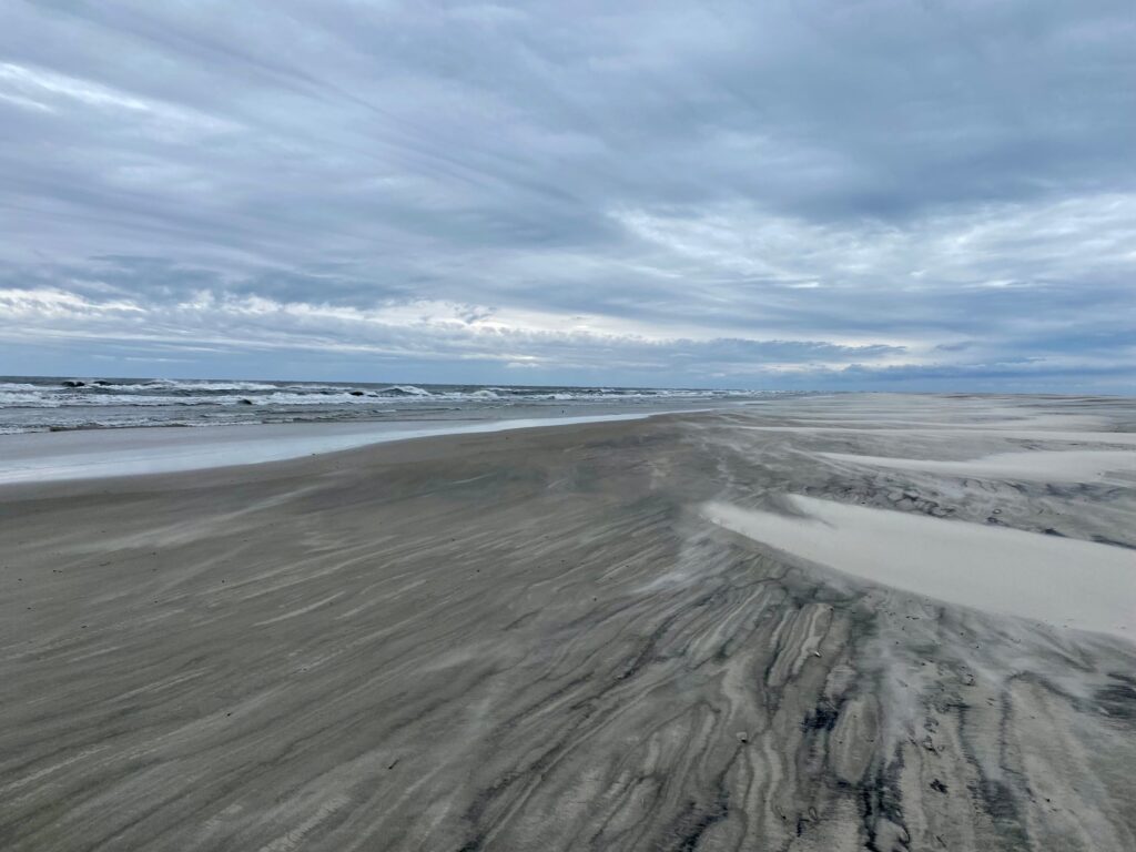 Wind-blown sand and shallow water across the wide flats of South Point on Ocracoke Island.