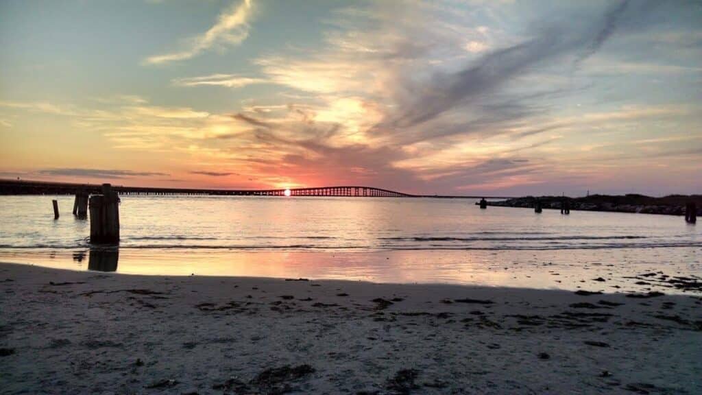 Sunset light glowing across calm water past a low pier at Cape Hatteras National Seashore.