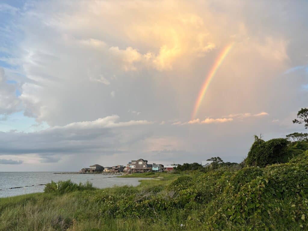 A rainbow in a bright evening sky above the trees and rooftops of Ocracoke Village.