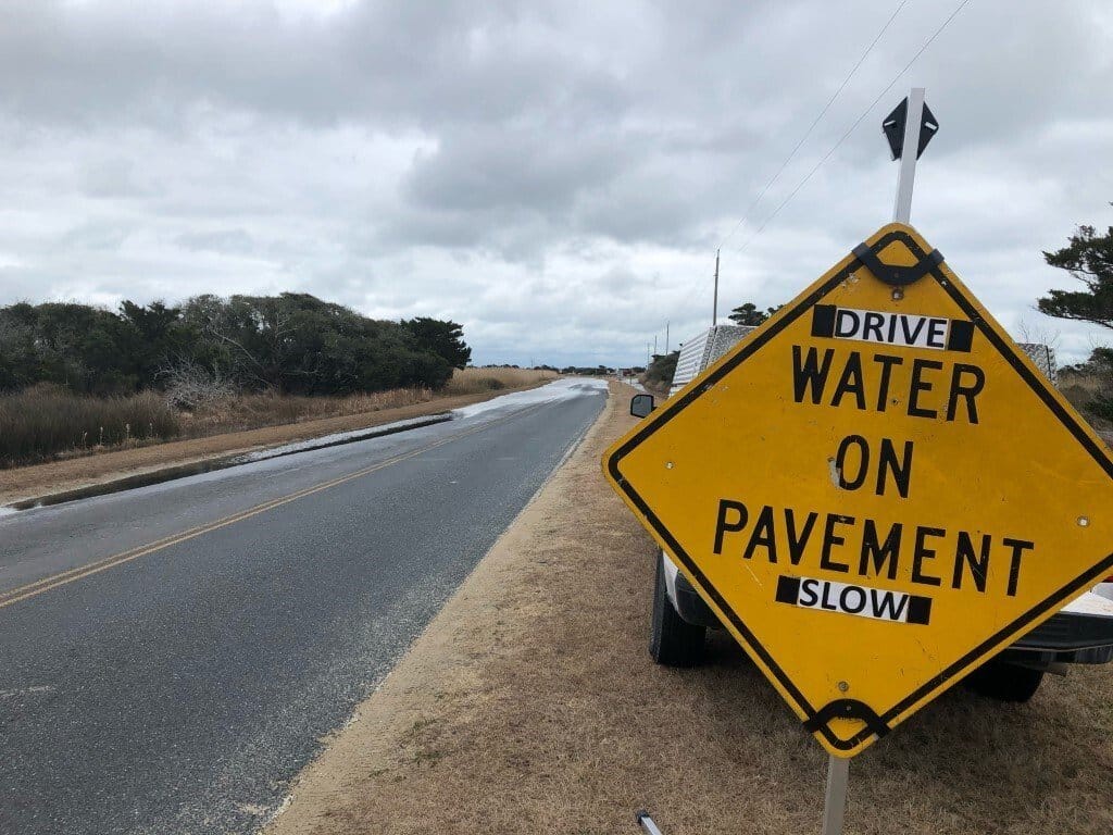 A yellow diamond road sign reading Water On Pavement beside NC Highway 12.