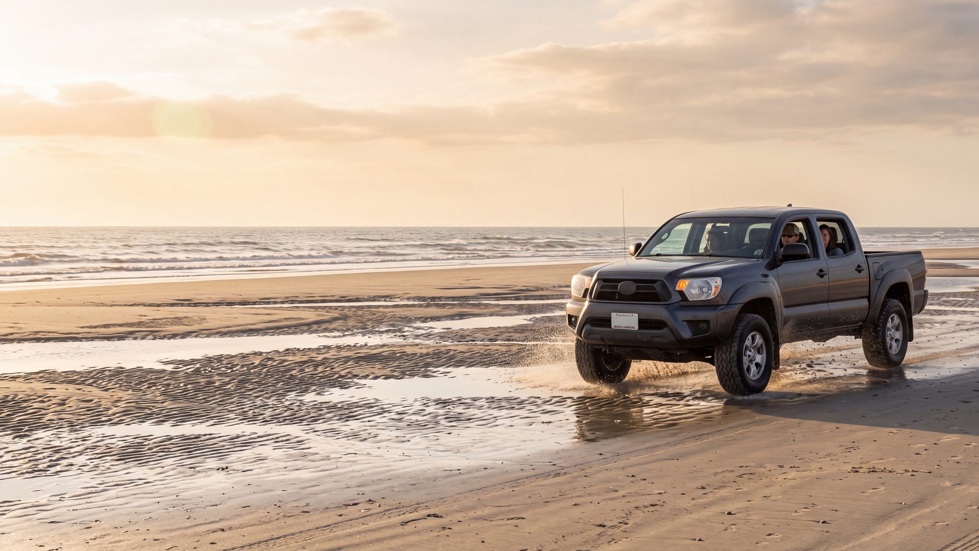 A 4x4 truck driving on the wide hard-packed sand of a dead-low tide with exposed sandbars — Outer Banks, NC