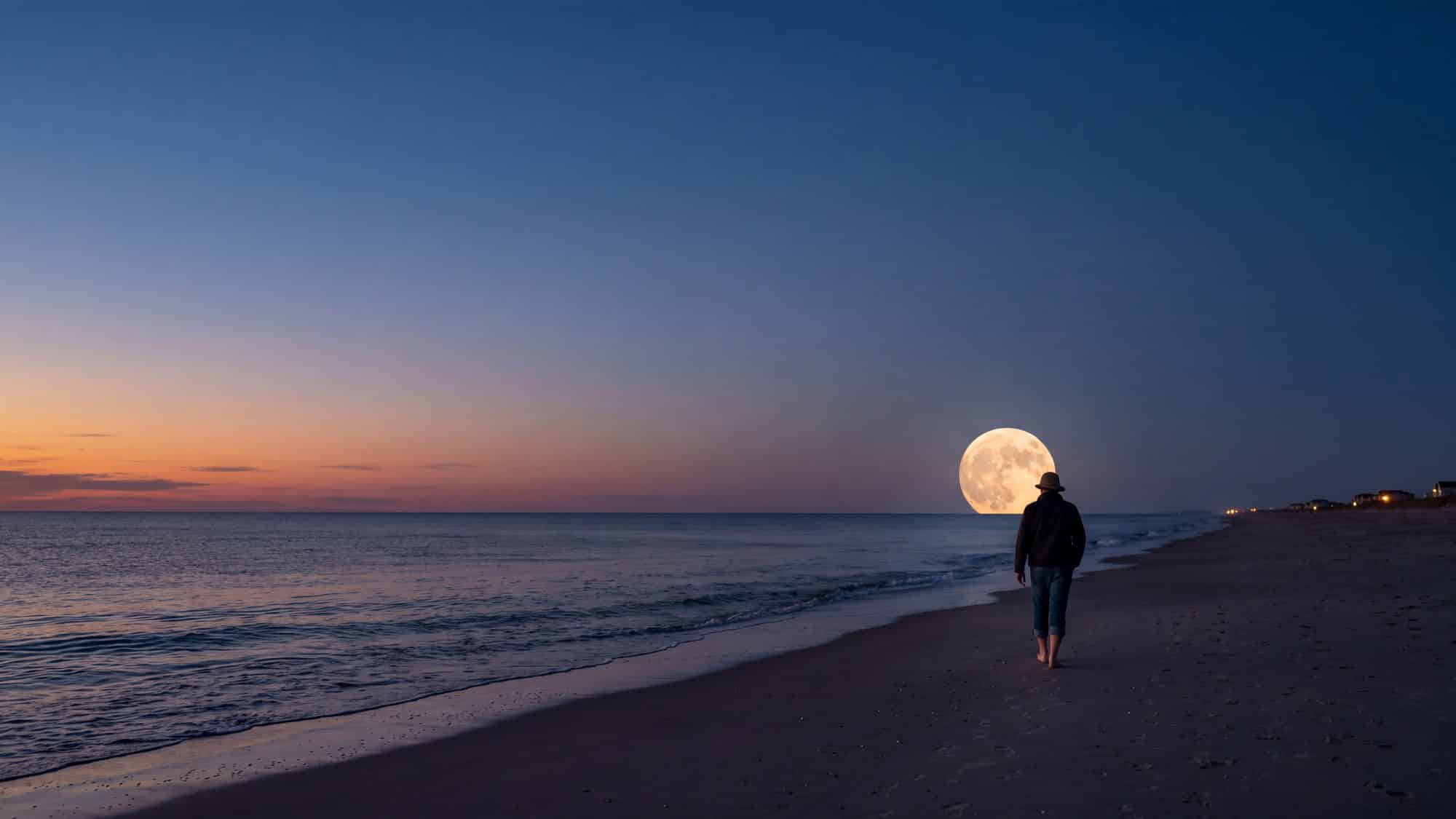 A full moon rising over the ocean at dusk above a calm wide beach — Outer Banks, NC