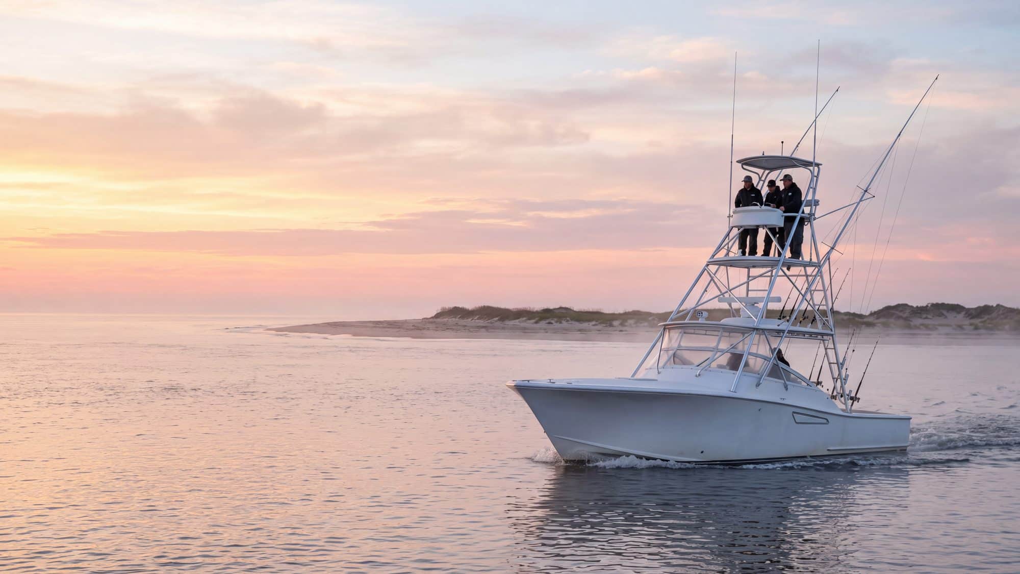 A white sportfishing boat with a tuna tower running out through an inlet at first light — Outer Banks, NC