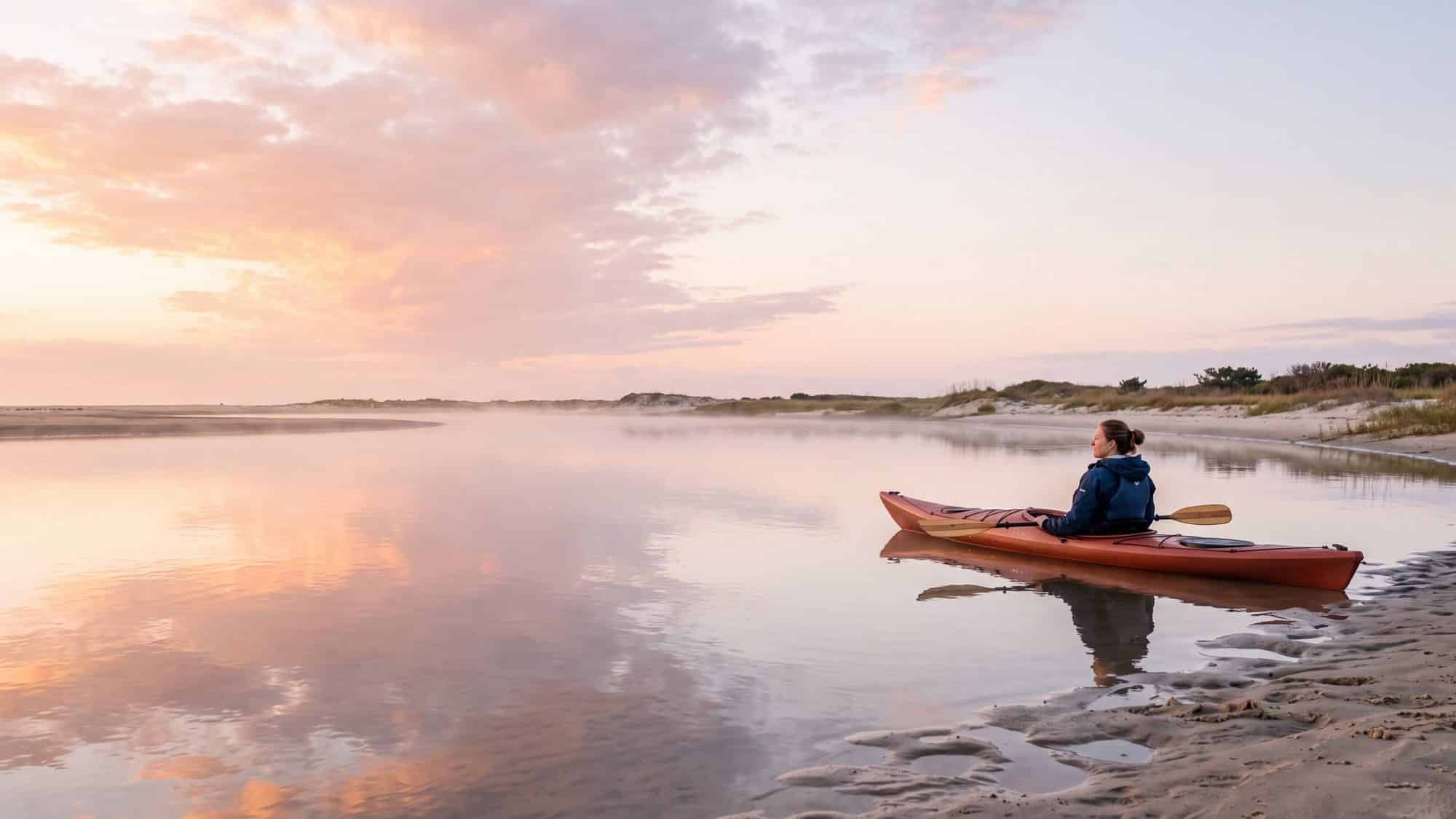 Perfectly still glassy water in a sandy inlet at slack tide with a kayaker resting — Outer Banks, NC