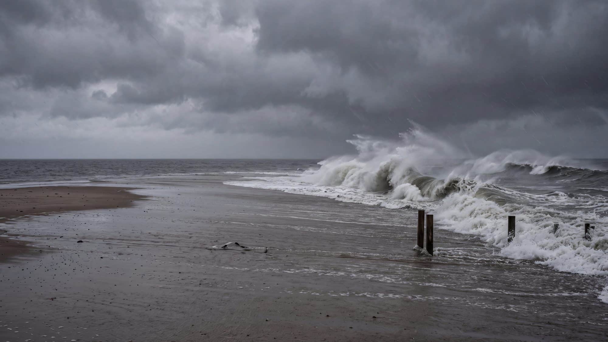 Heavy grey surf breaking high up an empty beach under a dark storm sky — Outer Banks, NC